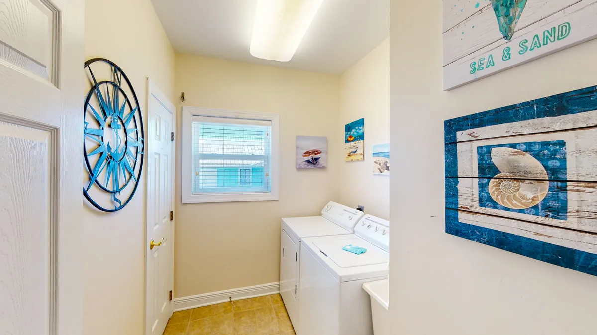 A bright laundry nook featuring a modern washing machine, decorative nautical wall art, and a cheerful blue clock. Natural light streams in, illuminating the space and emphasizing the sense of cleanliness and freshness.