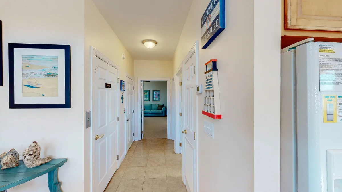A wide hallway leads into a vibrant, welcoming living area filled with colorful decor and framed artwork. The open plan hints at easy movement between spaces and a thoughtful, accessible layout ideal for greeting guests or transitioning between the home’s different areas.