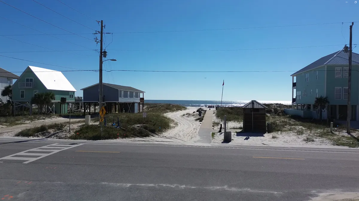 This image features a beach access path leading toward the sparkling ocean, flanked by colorful beach houses. The sand appears inviting and the ocean horizon is visible, while the tranquil setting hints at family-friendly activities like beach walks and sandcastle building.