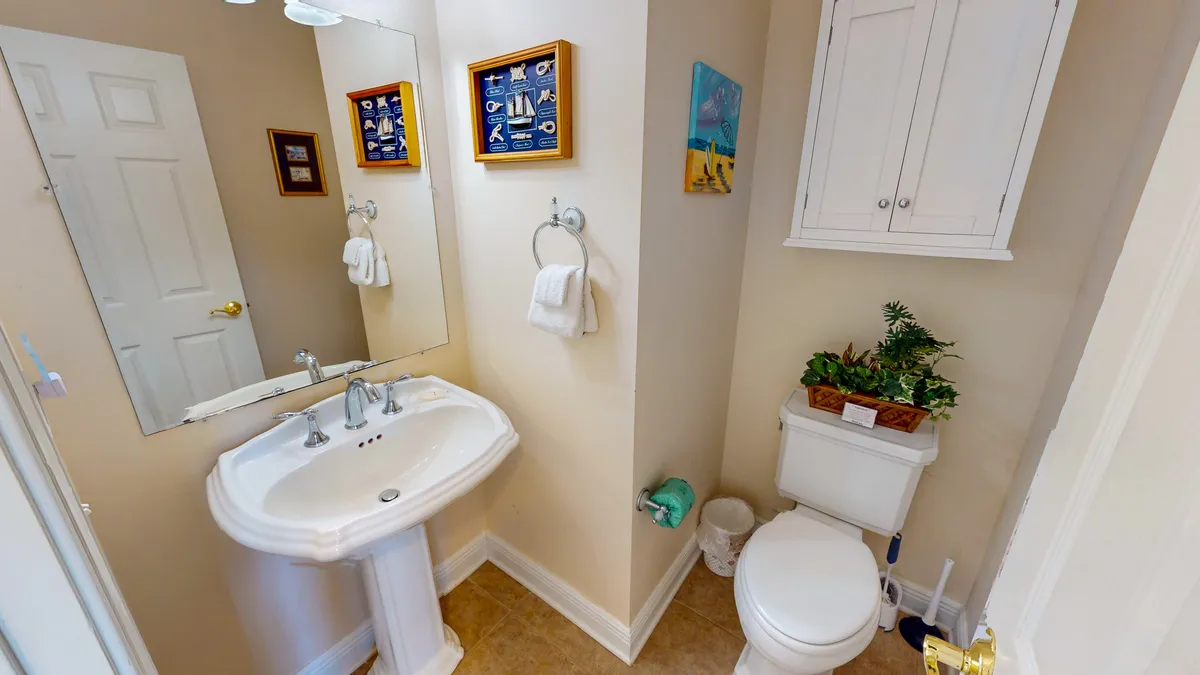 This image presents a stylish half bath with a sink, toilet, decorative art, towels, and a small plant. The mood is calm and inviting, suggesting comfort and convenience for guests during gatherings.